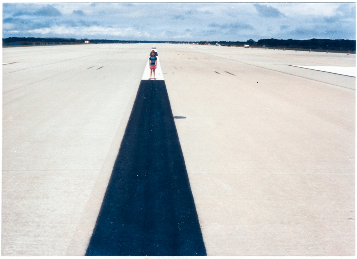 Kai MacLaren stands on the centerline of the 15,000-foot runway at the Shuttle Landing Facility, Kennedy Space Center, Florida. Behind him, the entire length of the runway extends out beyond sensible vision, to the north. This is where Space Shuttle missions that returned to their launch site touched down, shortly after the double-thunderclap of the sonic boom they created had echoed across the land. This is where their full weight, imposed by earth’s gravity, was once again re-impressed upon the astronauts who would disembark from the orbiter, at mission’s end. This was the End, that enabled the next Beginning.